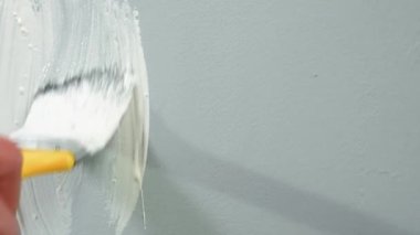 The unrecognizable man paints a gray wall with white paint using a yellow brush. Close up of a hand of painter or repairman sliding a brush over a wall and painting over it. The concept of repair