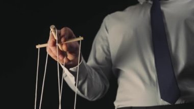 Beyaz gömlekli ve siyah kravatlı bir işadamı tahta manipülatörü ve ipleri olan bir kuklayı kontrol ediyor. Bir kuklacı, siyah izole edilmiş arka planda bir kuklayı kontrol eder. Kontrol konsepti