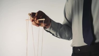 Gri gömlekli ve siyah kravatlı bir işadamı tahta manipülatörü ve ipleri olan bir kuklayı kontrol ediyor. Bir kuklacı, beyaz izole bir arkaplanda oyuncak bir kuklayı kontrol eder. Kontrol konsepti