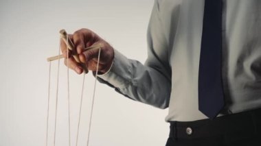 A businessman in a gray shirt and black tie controls a puppet with a wooden manipulator and strings. A puppeteer controls a doll marionette on a white isolated background. The concept of control