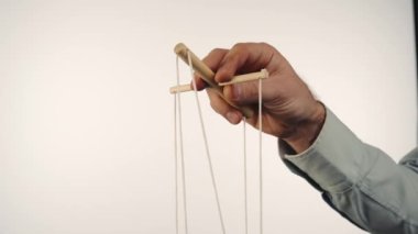 The hand of a man in a gray shirt controls a puppet using a wooden manipulator and strings. Hand handling at puppet by pulling strings to make the character move. Concept of mind manipulation, boss