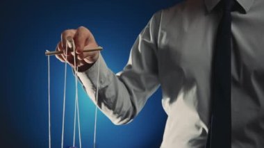 Gri gömlekli ve siyah kravatlı bir işadamı tahta manipülatörü ve ipleri olan bir kuklayı kontrol ediyor. Karakteri hareket ettirmek için ipleri elinde tutarak kuklada el muamelesi yapıyorsun. Mavi izole arkaplan