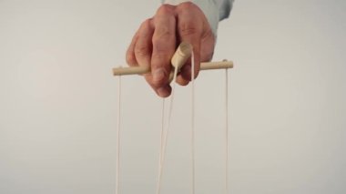 The puppeteers hand controls the puppet with a wooden manipulator and strings. The marionettist controls and pulls the strings on a white isolated background. Concept of dependence, dominance