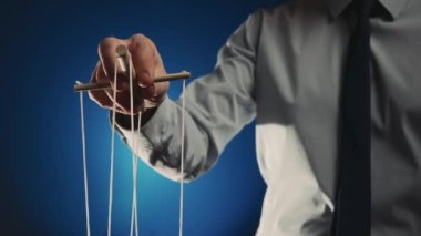 Gri gömlekli ve siyah kravatlı bir işadamı tahta manipülatörü ve ipleri olan bir kuklayı kontrol ediyor. Karakteri hareket ettirmek için ipleri elinde tutarak kuklada el muamelesi yapıyorsun. Mavi izole arkaplan