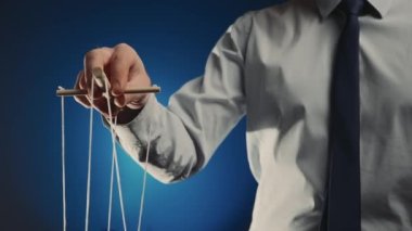 Gri gömlekli ve siyah kravatlı bir işadamı tahta manipülatörü ve ipleri olan bir kuklayı kontrol ediyor. Karakteri hareket ettirmek için ipleri elinde tutarak kuklada el muamelesi yapıyorsun. Mavi izole arkaplan