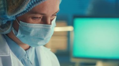Portrait of a woman in a medical mask, bonnet and white coat works intently. Doctor, laboratory assistant or researcher in a biochemical laboratory or hospital. The concept of medicine, healthcare