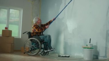 Tekerlekli sandalyedeki yaşlı bir adam uzun bir silindirle bir duvarı beyaz boyayla boyuyor. Bu yaştaki engelli bir adam odada tamirat yapar. Apartmandaki tamirat konsepti...