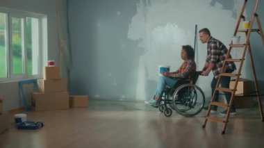 Beyaz bir adam, elinde bir kova boyayla Afrikalı Amerikalı bir kadını tekerlekli sandalyedeki bir odaya götürüyor. Bir erkek, boyayı dökmemek için dengesini koruyan bir kadını neşeyle yuvarlar. A
