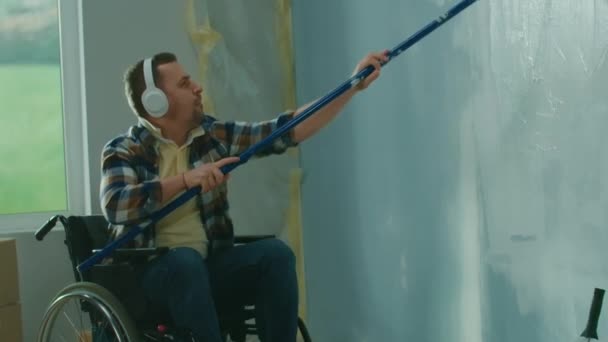 Młody Mężczyzna Białych Słuchawkach Wózku Inwalidzkim Maluje Ścianę Białą Farbą — Wideo stockowe