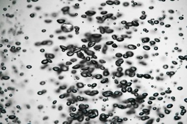 A lot of shiny dark air bubbles of different sizes underwater on a white isolated background. Close up of light lit oxygen bubbles flow upwards. Aeration or filtration of liquid. Fizzy flow of air