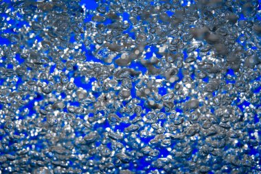 A lot of shiny air bubbles of different sizes underwater on a blue background. Close up of light lit oxygen bubbles flow upwards. Aeration or filtration of liquid. Fizzy stream of air bubbles
