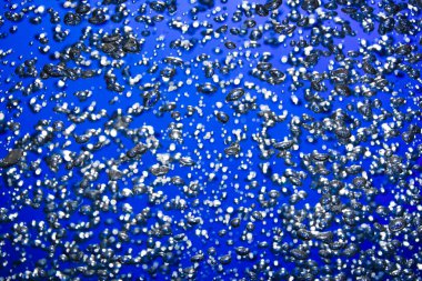 A lot of shiny air bubbles of different sizes underwater on a blue background. Close up of light lit oxygen bubbles flow upwards. Aeration or filtration of liquid. Fizzy stream of air bubbles
