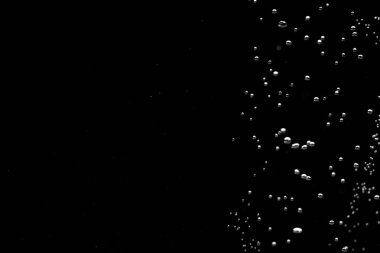 Shiny air bubbles in the right side of the frame on a black isolated background. Background with oxygen bubbles and workspace, mockup. Close up of a bubbling liquid. Fizzy flow of air bubbles