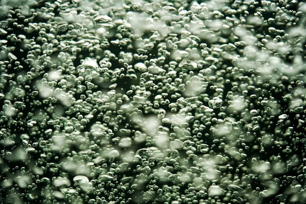 A stream of shiny air bubbles illuminated by light and shining on a dark background. Close up of light lit oxygen bubbles flow upwards. Aeration or filtration of liquid. Fizzy flow of air bubbles
