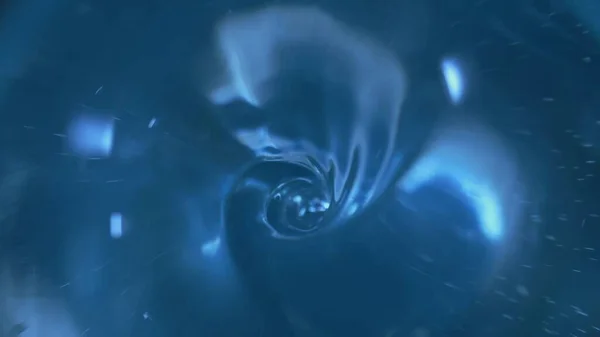 The surface of clear blue water swirls into a whirlpool and a funnel is formed. Swirl of a transparent liquid. Draining water, leaking in the bathroom or sink. A round hole from a water vortex is