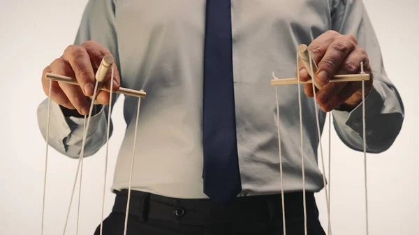 stock image A businessman in a gray shirt and black tie controls a puppet with a wooden manipulator and strings. The puppeteer manipulates the puppet by pulling the ropes with both hands on a white background