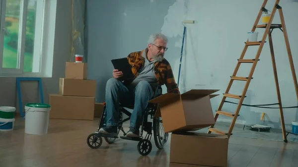 Vanhempi Vammainen Mies Muuttaa Pyörätuolilla Suunnittelemaan Remonttia Digitaalisen Tabletin Avulla — kuvapankkivalokuva