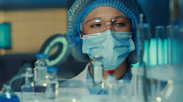 여인의 유리병 시험관을 검사한다 실험실이나 병원에서 광선을 마스크 장갑을 연구원들 — 스톡 사진