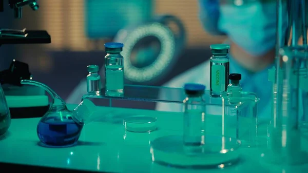 ガラス製の試験管 フラスコ ワクチンや薬でバイアルを保管してください 青色の光を持つ研究室や病院の医療事務所 背景には女性医師がいます 薬の概念 — ストック写真