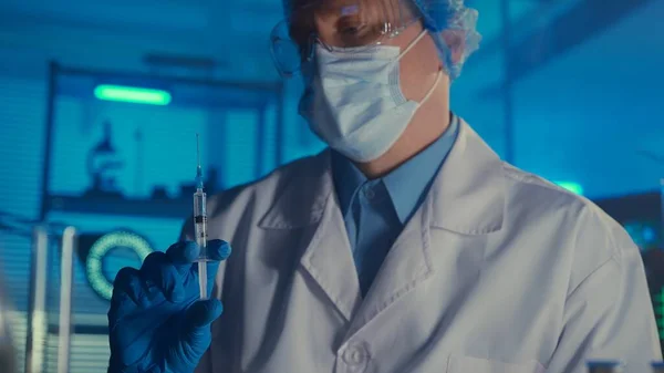 头戴白色外套 医疗面罩 护目镜和蓝色手套的男子手里拿着注射器 手里拿着疫苗或药品 现代生化研究实验室 制定一项创新的 — 图库照片