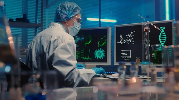 一个穿着白色长袍的男人在电脑键盘上打字 一位男性研究人员 背景在一个配备了试管 瓶和显微镜的现代实验室 医疗发展实验室 生物化学 — 图库照片
