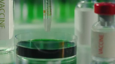 Cam pipet, petri kabından çıkan yeşil sıvıyla doludur. Masanın yanında aşı ya da ilaç içeren cam şişeler var. Laboratuvardaki biyokimyasal araştırma kavramı. Modern biyokimyasal