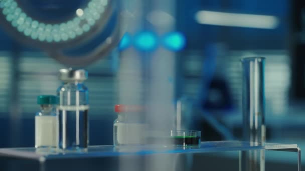 一滴清澈的液体从玻璃杯里滴到一个有绿色物质的培养皿里 桌面上放着装有疫苗或药物的玻璃瓶 生物化学研究的概念 — 图库视频影像