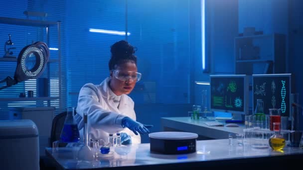 アフリカ系アメリカ人の女性が仮想グラフィックを調べ 写真をズームします 黒人女性医師や研究者は 青色光を用いた生化学的現代研究室で働いている コンピュータグラフィックスや場所 — ストック動画