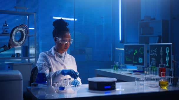 アフリカ系アメリカ人の女性が仮想グラフィックを調べ ズームし 画像をスワイプします 黒人女性医師や研究者は 青色光を用いた生化学的現代研究室で働いている コンピュータの場所 — ストック動画
