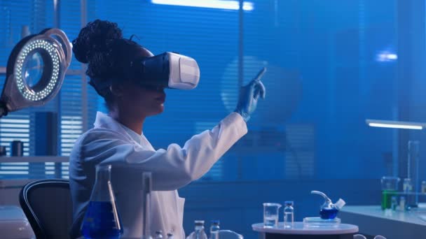 非洲裔美国妇女在虚拟现实耳机检查样品 滚动图像 黑人女医生或研究人员在蓝光的生化现代实验室工作 — 图库视频影像
