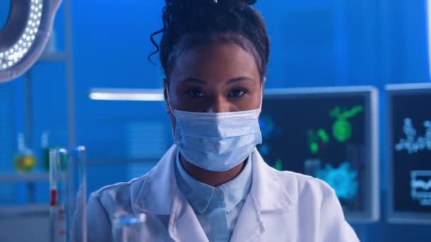 若いアフリカ系アメリカ人女性がカメラを見て保護医療マスクを外し 安堵のため息をつく 現代の白い医療用ガウンを着た黒人女性医師の肖像 — ストック動画