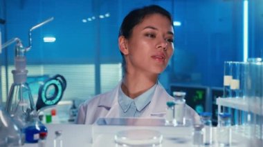 Asyalı kadın doktor bir test tüpü alıp işaretliyor. Beyaz önlüklü Koreli kadın laboratuvar asistanı laboratuarda ya da mavi ışığı olan bir hastanede. Cam şişelerle dolu bir raftan bak
