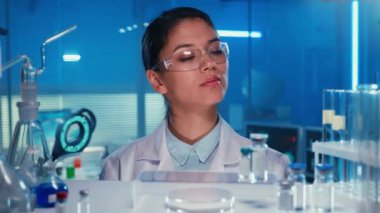 Asyalı kadın doktor bir test tüpü alıp işaretliyor. Beyaz önlüklü Koreli kadın laboratuvar asistanı laboratuarda ya da mavi ışığı olan bir hastanede. Cam şişelerle dolu bir raftan bak