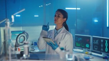 Asyalı doktor dijital tablet kullanır, envanter çıkarır ya da ilaç sipariş eder. Beyaz tıbbi önlüklü, Kore uyruklu bir kadın laboratuvar asistanı. Laboratuvar ya da hastane. Mavi ışık, cam.