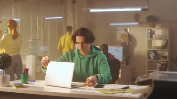 Молодий Чоловік Друкує Клавіатурі Ноутбука Сидячи Столом Офісі Задньому Плані — стокове відео