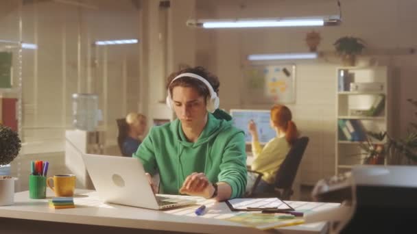 Молодой Человек Белых Больших Наушниках Печатает Клавиатуре Ноутбука Наслаждается Музыкой — стоковое видео