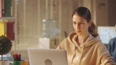 Bej eşofmanlı genç bir kadının portresi dizüstü bilgisayarda klavyeye yazı yazıp kameraya bakıyor ve gülümsüyor. Bir kadın yönetici ya da programcı parlak bir ofiste bir masada oturur. Ofis işi