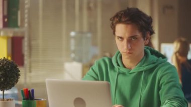 Yeşil kazaklı bir gencin portresi dizüstü bilgisayarda klavyeye yazı yazıp kameraya bakıyor ve gülümsüyor. Bir erkek yönetici ya da programcı parlak bir ofiste bir masada oturur. Ofis işleri ve...
