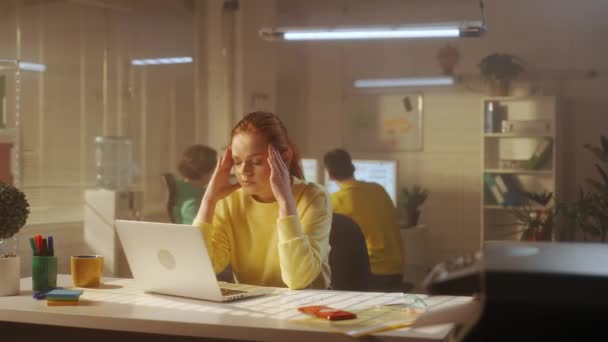 黄色のパーカーを着た怒り狂った女性が報告書を確認し 怒って紙を砕き捨てます 背景には若いクリエイティブチームが働いています 事務所 — ストック動画