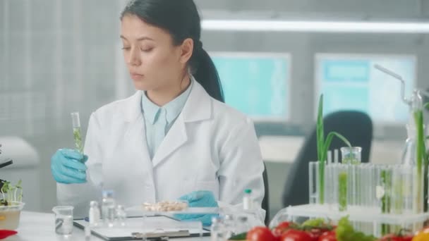 亚洲女性研究人员将液体注入带有绿色幼苗的试管 并做笔记 微生物学家分析产品的质量 绿芽的研究 基因改造 — 图库视频影像