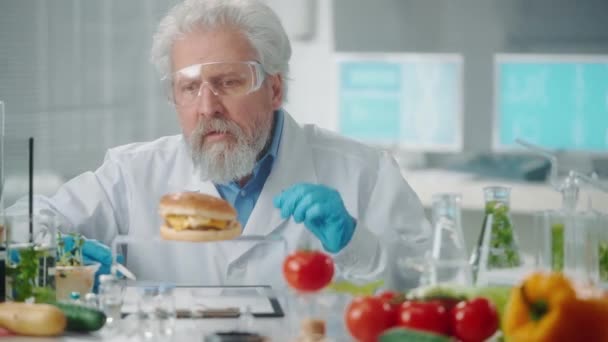 Ηλικιωμένος Άνδρας Ερευνητής Εξετάζει Ένα Δείγμα Του Burger Και Γράψει — Αρχείο Βίντεο