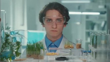 Beyaz önlüklü ve gözlüklü bir biyoteknoloji uzmanı kameraya bakıp gülümsüyor. Bitkilerin matara ve test tüplerinde yetişen yeşil filizleri. Laboratuvarda yetişen yeşil lahanalarla biyoloji deneyi.