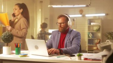 Orta yaşlı sakallı bir adam dizüstü bilgisayarda yazı yazıyor ve büyük beyaz kulaklıklarla müziğin tadını çıkarıyor. Mavi ceketli ve kırmızı balıkçı yakalı bir işadamı ofiste bir masada oturuyor. Şey...