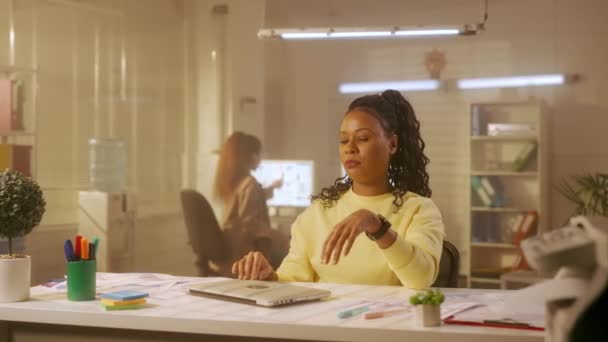 年轻的非洲裔美国女人合上笔记本电脑 摆出一副镇静自若的姿势放松下来 穿着黄色运动衫的黑人女程序员或设计师坐在办公室的桌子旁 管理团队正在工作 — 图库视频影像