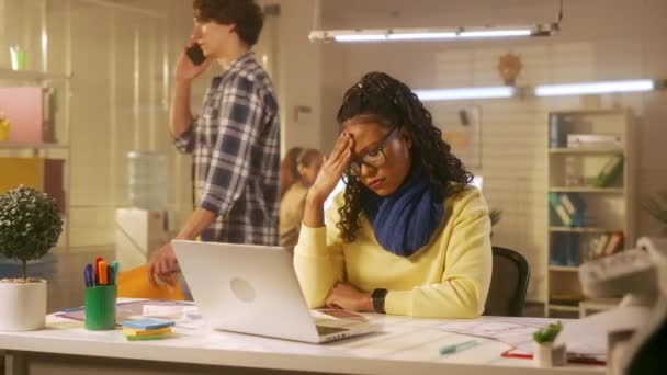 若いアフリカ系アメリカ人女性がノートパソコンのキーボードを入力しており 喉の痛みや咳に苦しんでいます 首にスカーフを被った黒人女性がオフィスのテーブルに腰を下ろしている — ストック動画