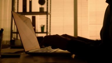 Laptop klavyesine yazı yazan bir adamın karanlık yüzü. Siyah gömlekli bir erkek yönetici, tasarımcı ya da programcı akşamları karanlık bir ofiste masada otururken çalışır. Eller ve