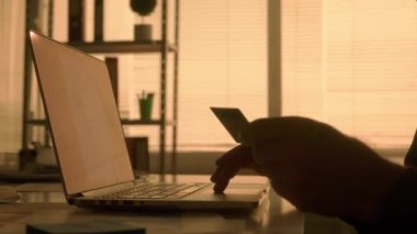 İnternetten bilgisayarla ve banka kartıyla online alışveriş yapan bir adamın karanlık yüzü. Siyah gömlekli bir erkek yönetici, tasarımcı veya programcı masada otururken çalışır.