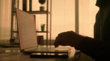 Laptop klavyesine yazı yazan ve cep telefonuyla mesajlaşan bir adamın karanlık görüntüsü. Siyah gömlekli bir erkek yönetici, tasarımcı veya programcı karanlıkta bir masada otururken çalışır.