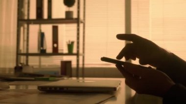 Bir adamın karanlık silueti cep telefonunun ekranında bilgiyi araklayıp yakınlaştırıyor. Siyah gömlekli bir erkek yönetici, tasarımcı veya programcı karanlıkta bir masada otururken çalışır.