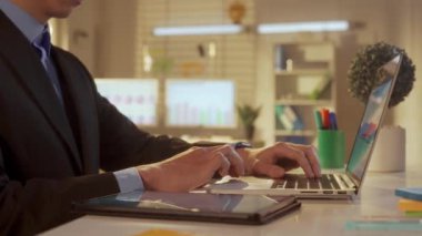 Laptop ve tablet üzerinde çalışan takım elbiseli genç bir adamın yan görüntüsü. Bir yönetici, yönetici, programcı ya da işadamı dizüstü bilgisayarda klavye kullanıyor ve bir tablete not alıyor. Ofis işi